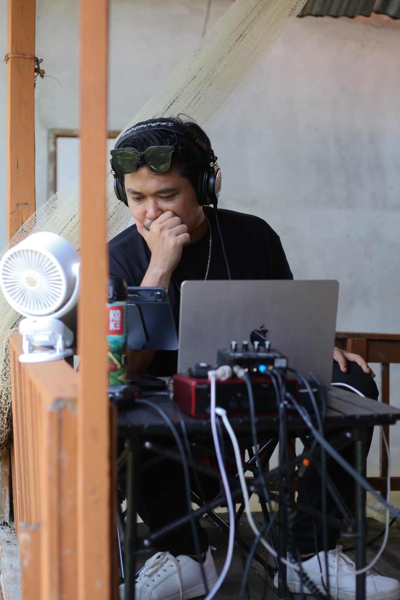 Eka bekerja dengan laptop, headphone, dan perangkat audio.